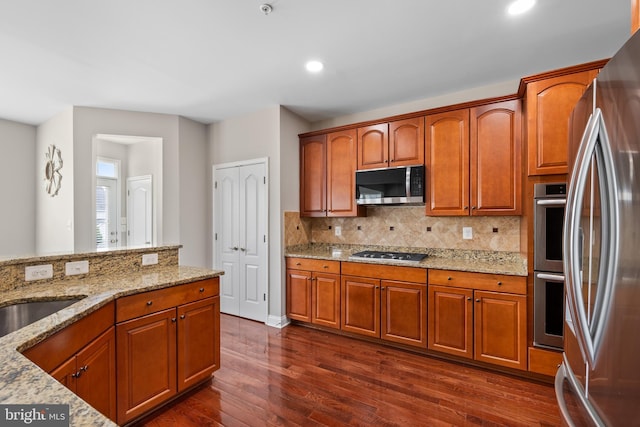kitchen with appliances with stainless steel finishes, dark wood-style flooring, backsplash, and light stone counters