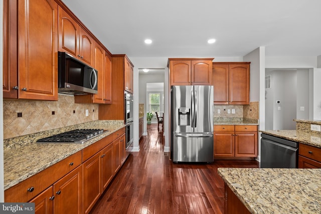 kitchen featuring stainless steel appliances, backsplash, light stone countertops, dark wood-style floors, and brown cabinetry