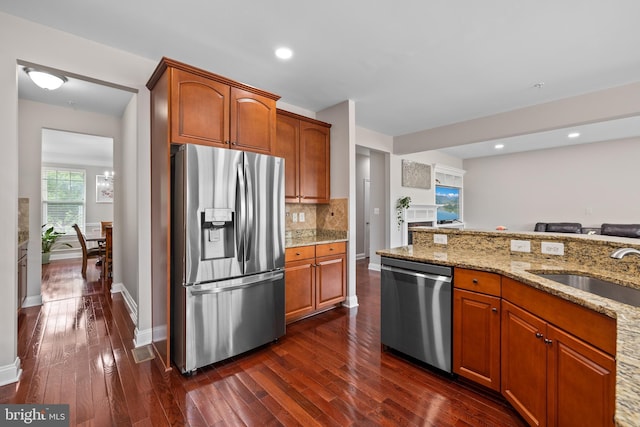 kitchen with dark wood finished floors, decorative backsplash, appliances with stainless steel finishes, a sink, and light stone countertops