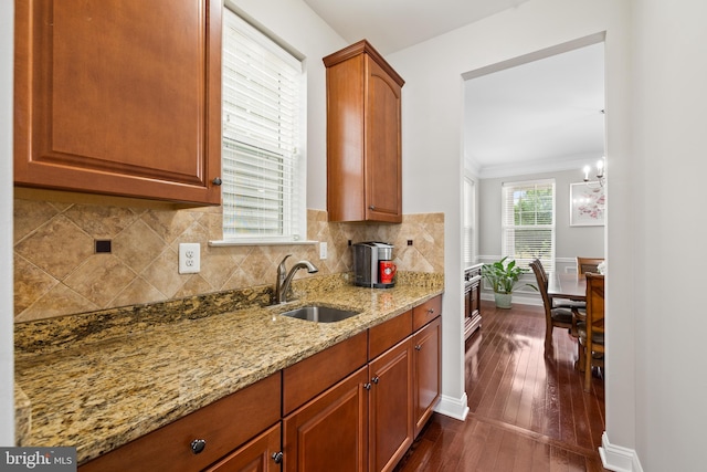 kitchen with light stone counters, dark wood-style flooring, a sink, decorative backsplash, and crown molding