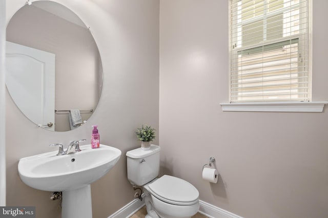 half bath featuring baseboards and toilet