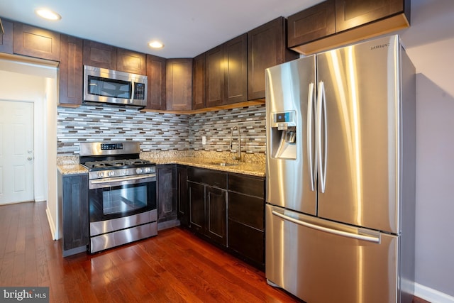 kitchen with tasteful backsplash, sink, light stone countertops, and appliances with stainless steel finishes