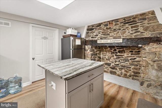 kitchen featuring light hardwood / wood-style flooring, stainless steel fridge, gray cabinets, a center island, and light stone counters