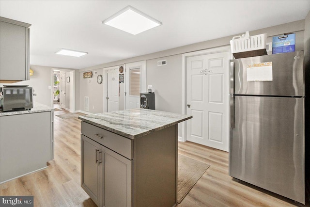 kitchen with gray cabinetry, stainless steel fridge, a center island, light stone countertops, and light hardwood / wood-style flooring