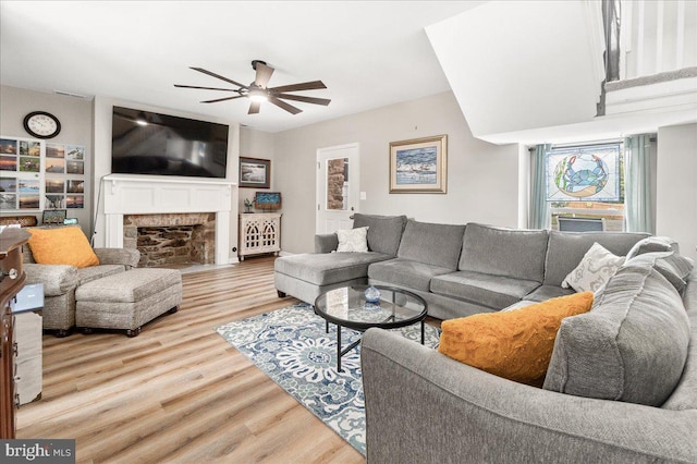 living room featuring ceiling fan, a brick fireplace, and light wood-type flooring