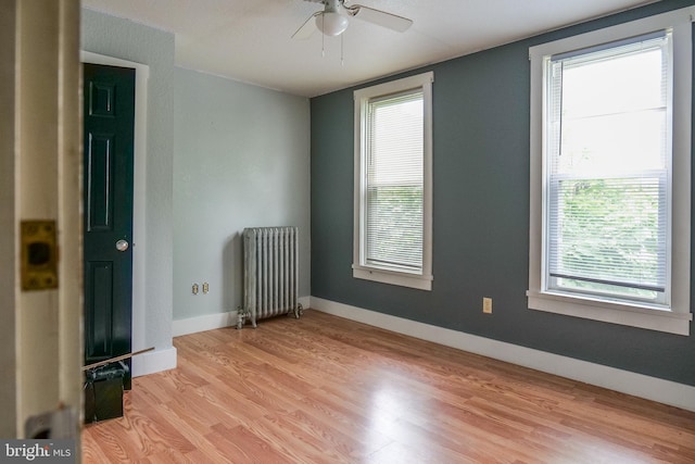 empty room with ceiling fan, a healthy amount of sunlight, light hardwood / wood-style floors, and radiator