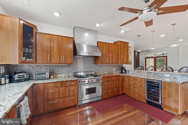 kitchen featuring kitchen peninsula, wall chimney exhaust hood, beverage cooler, decorative light fixtures, and high end stainless steel range