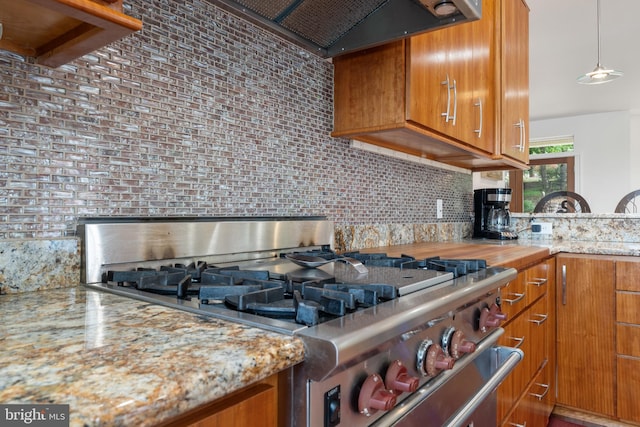 kitchen with stove, tasteful backsplash, light stone counters, custom range hood, and decorative light fixtures