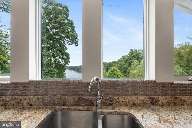 interior details featuring a water view, dark stone countertops, and sink