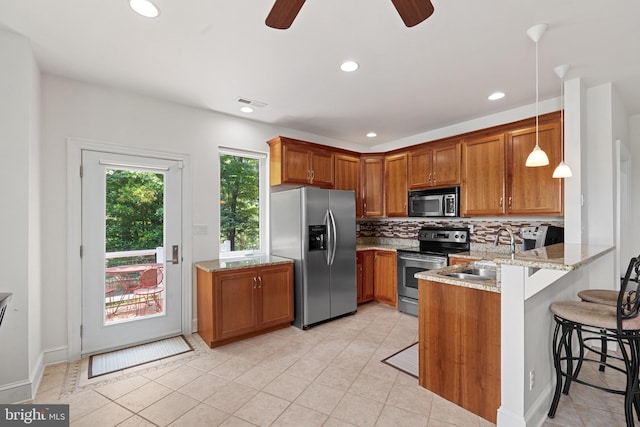 kitchen featuring kitchen peninsula, stainless steel appliances, sink, pendant lighting, and a breakfast bar area