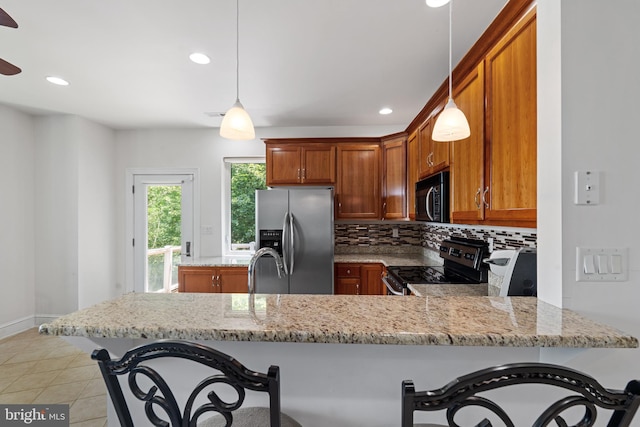 kitchen with hanging light fixtures, stainless steel appliances, light stone counters, backsplash, and kitchen peninsula