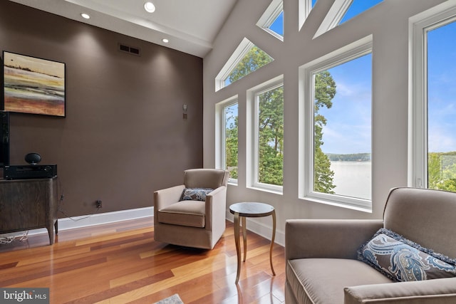 sitting room featuring a water view, light wood-type flooring, and vaulted ceiling