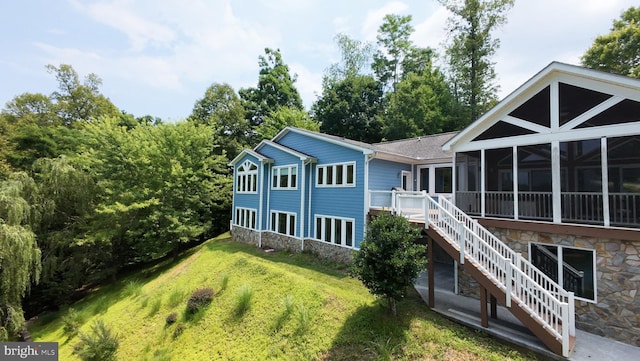 rear view of property featuring a deck, a lawn, and a sunroom