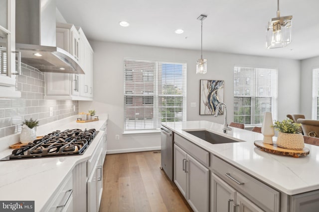 kitchen with a wealth of natural light, sink, wall chimney exhaust hood, decorative light fixtures, and appliances with stainless steel finishes