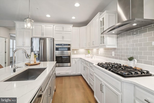 kitchen with white cabinets, wall chimney range hood, sink, decorative light fixtures, and stainless steel appliances