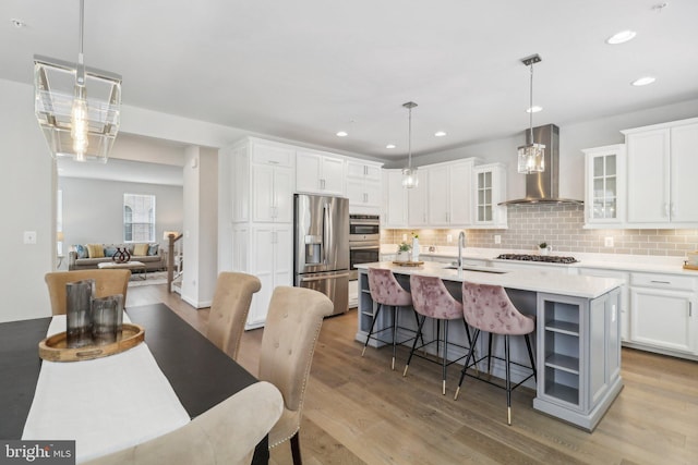 kitchen featuring pendant lighting, white cabinets, wall chimney range hood, and appliances with stainless steel finishes