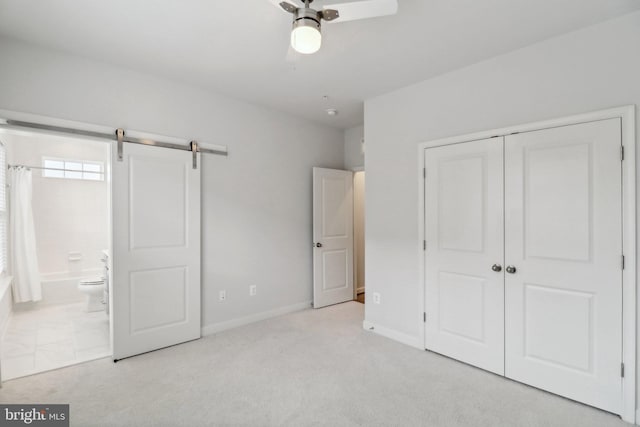 unfurnished bedroom featuring ensuite bathroom, ceiling fan, a barn door, light colored carpet, and a closet