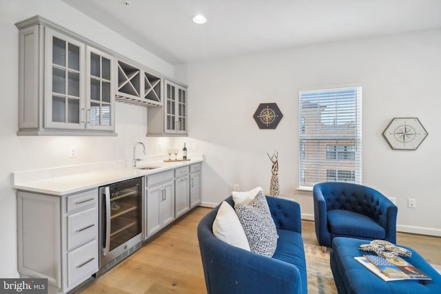 bar featuring wine cooler, sink, gray cabinetry, and light hardwood / wood-style flooring