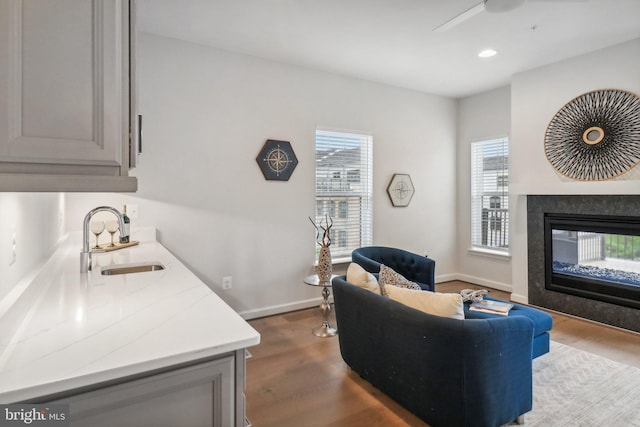 living room featuring a multi sided fireplace, ceiling fan, sink, and wood-type flooring