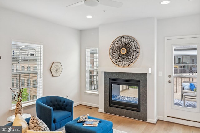 living room with a multi sided fireplace, light hardwood / wood-style flooring, and ceiling fan