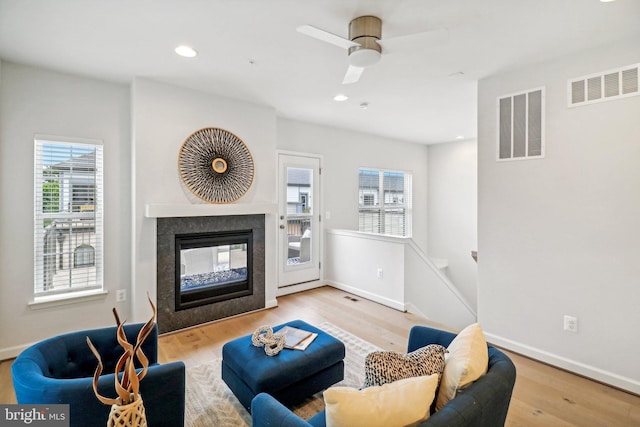 living room featuring ceiling fan, a multi sided fireplace, and light hardwood / wood-style flooring