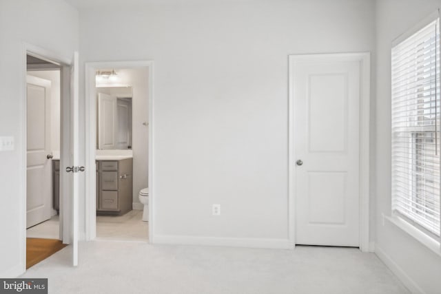 unfurnished bedroom featuring ensuite bathroom and light colored carpet