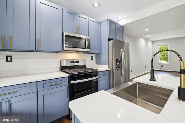 kitchen featuring tasteful backsplash, light stone counters, stainless steel appliances, sink, and blue cabinetry