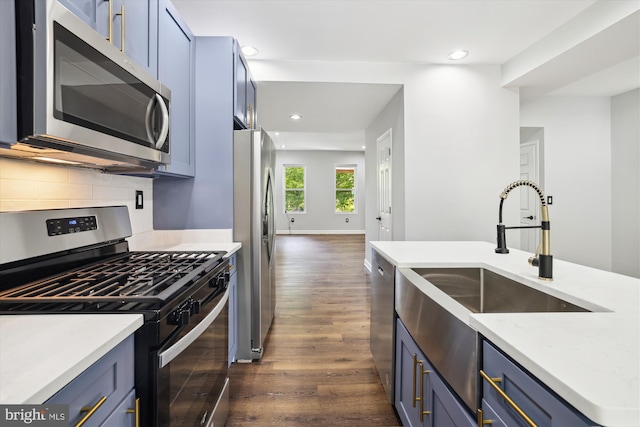 kitchen with sink, blue cabinets, dark wood-type flooring, and appliances with stainless steel finishes