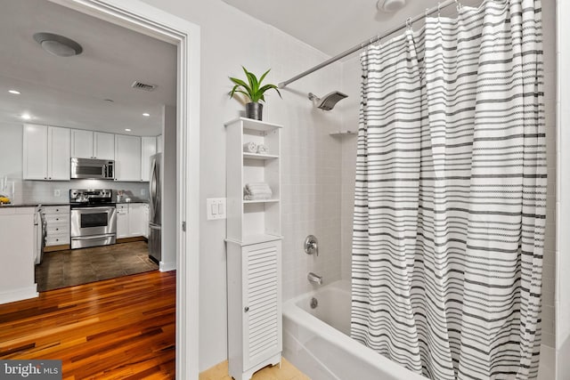 bathroom with hardwood / wood-style flooring, shower / bathtub combination with curtain, and tasteful backsplash