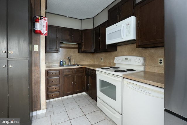 kitchen featuring dark brown cabinets, light countertops, light tile patterned floors, white appliances, and a sink