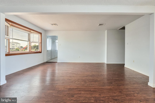 unfurnished room with a textured ceiling, wood finished floors, visible vents, and baseboards