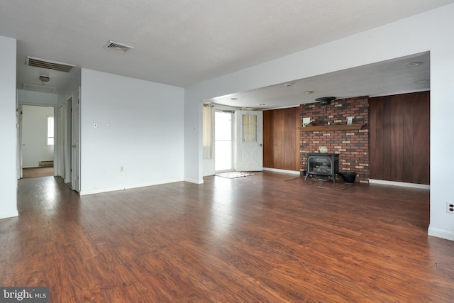 unfurnished living room with a wood stove, wooden walls, wood finished floors, and visible vents