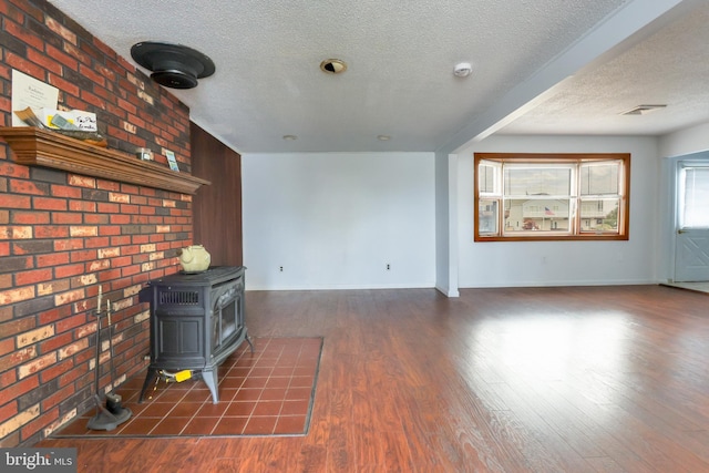 unfurnished living room with a wood stove, wood finished floors, visible vents, and baseboards