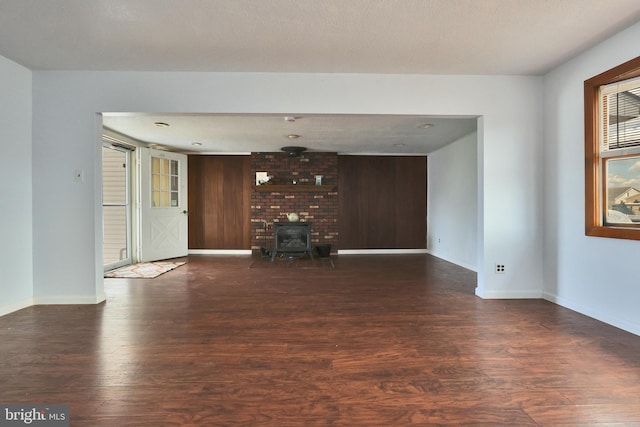 unfurnished living room featuring baseboards, wooden walls, wood finished floors, and a wood stove