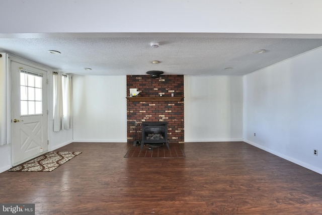 unfurnished living room featuring a textured ceiling, a wood stove, baseboards, and wood finished floors