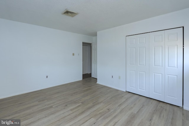 unfurnished bedroom with visible vents, wood finished floors, a closet, and a textured ceiling