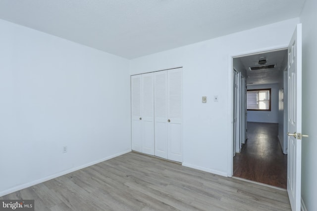 unfurnished bedroom with a closet, visible vents, baseboards, and wood finished floors