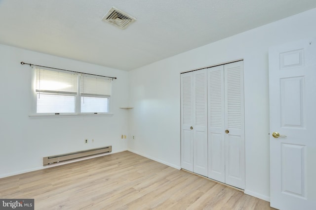 unfurnished bedroom with visible vents, a baseboard heating unit, baseboards, light wood-style floors, and a closet