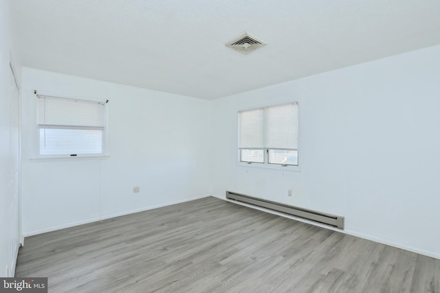 empty room featuring wood finished floors, visible vents, baseboard heating, and baseboards