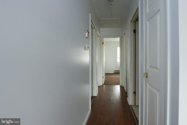 hall featuring attic access, a baseboard heating unit, baseboards, and dark wood-style flooring