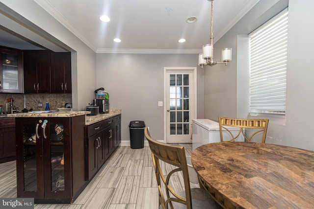 kitchen with light stone countertops, tasteful backsplash, a notable chandelier, dark brown cabinets, and ornamental molding