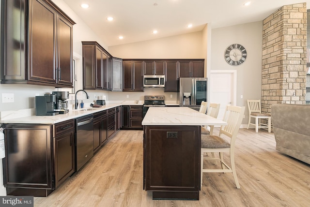 kitchen with sink, vaulted ceiling, light hardwood / wood-style floors, appliances with stainless steel finishes, and a kitchen island