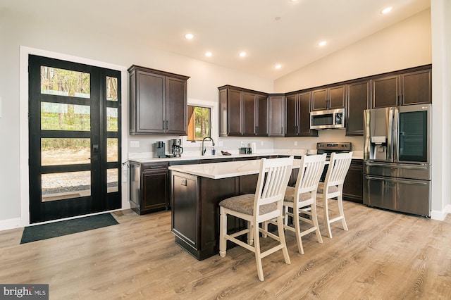 kitchen featuring a breakfast bar, a center island, lofted ceiling, appliances with stainless steel finishes, and light hardwood / wood-style floors