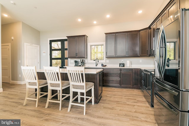 kitchen with stainless steel refrigerator, a center island, black range with electric cooktop, a kitchen bar, and light wood-type flooring