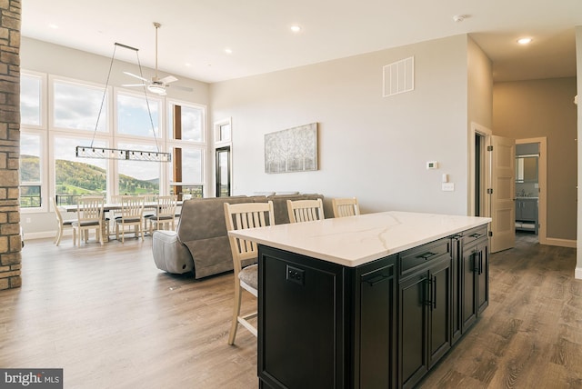 kitchen featuring ceiling fan, a center island, light stone countertops, a kitchen bar, and light wood-type flooring