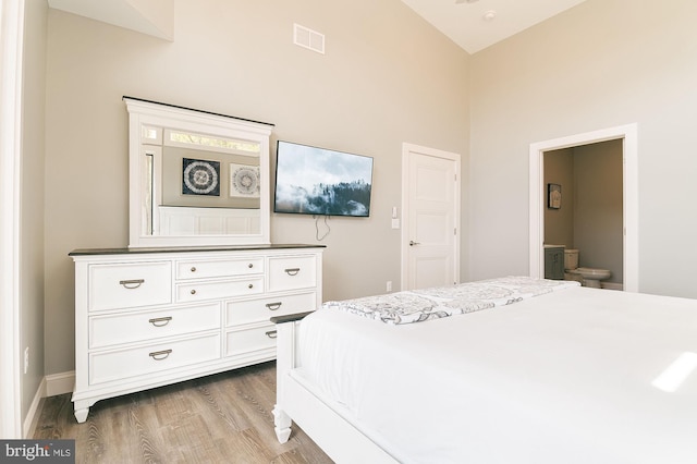 bedroom featuring ensuite bath, hardwood / wood-style floors, and high vaulted ceiling