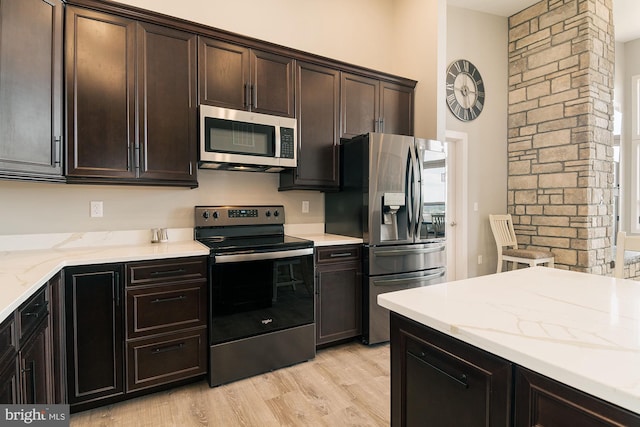 kitchen featuring light stone counters, dark brown cabinets, light hardwood / wood-style floors, and appliances with stainless steel finishes