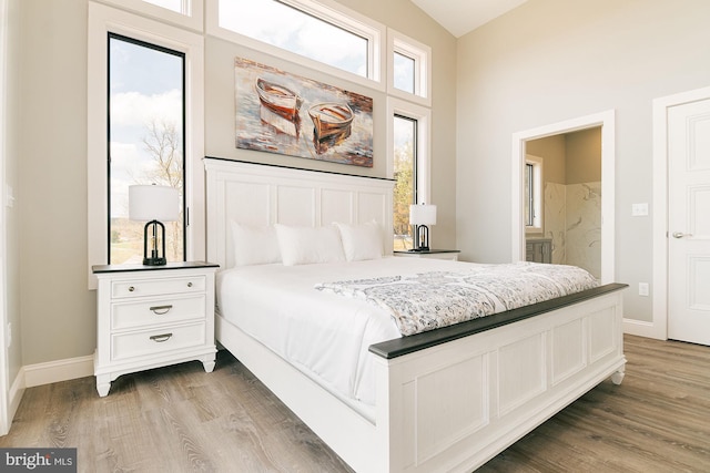 bedroom featuring wood-type flooring, lofted ceiling, and ensuite bath