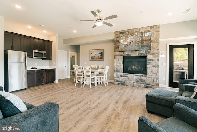 living room featuring ceiling fan, a fireplace, and light wood-type flooring