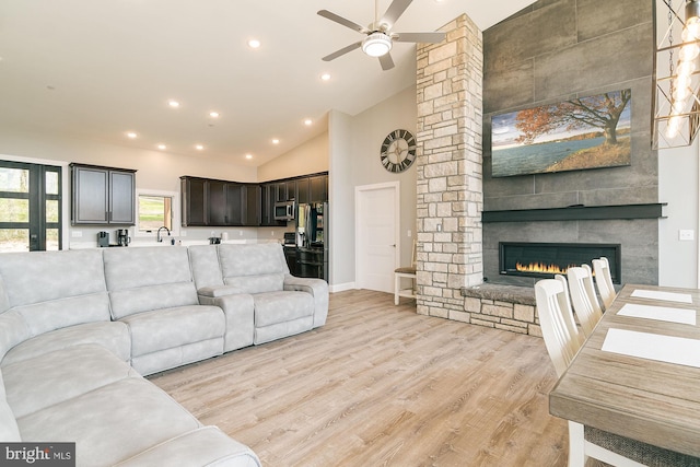 living room featuring a fireplace, light wood-type flooring, high vaulted ceiling, and ceiling fan